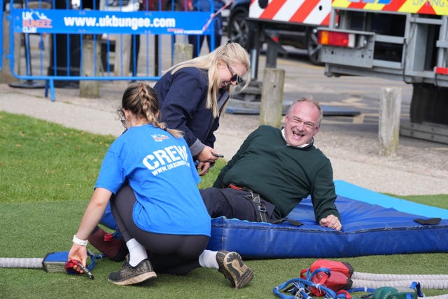 Sir Ed Davey on a blue mattress as two staff members help him out of his harness following a bungee jump