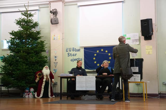 A man drops his vote into a ballot box, watched closely by voting overseers and Father Christmas