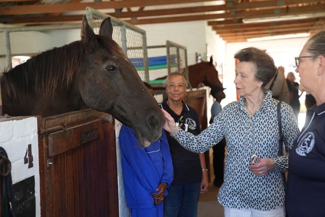 The Princess Royal pats a horse in the stables during a visit to the South African Riding School for Disabled Association 