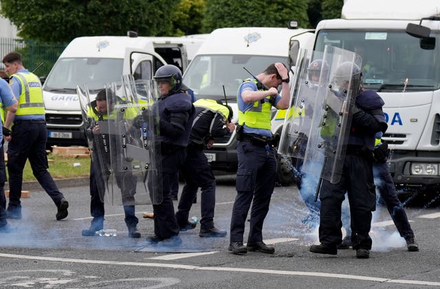 A line of gardai react as fireworks land at their position