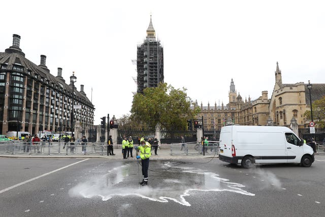 A street cleaner washes glue off the road outside the Palace of Westminster, London, following an Insulate Britain protest (James Manning/PA)