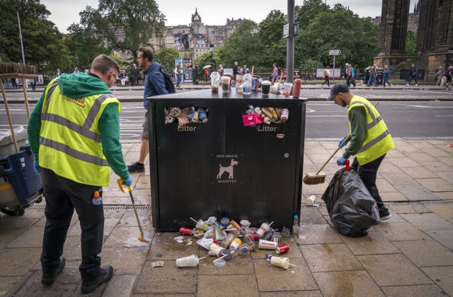 Shop workers picking up rubbish from an overflowing bin in Edinburgh