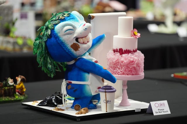 A cake which depicts a small blue creature smiling beside a mini cake