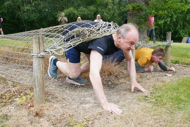 Liberal Democrats leader Sir Ed Davey crawling under netting on an assault course