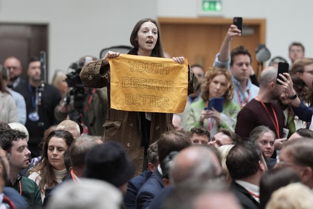 A protester holds a poster saying 'youth deserve better' while surrounded by members of the press and Labour Party supporters