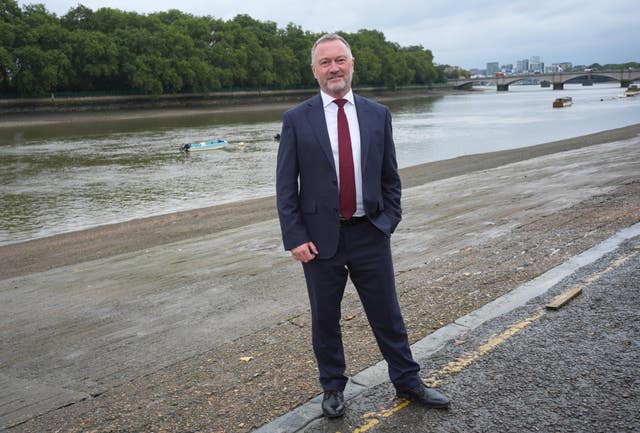 Steve Reed, wearing a suit and tie and standing next to a river