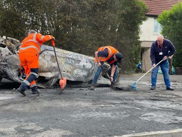 Council workers clear debris from the area immediately around a car that was set alight in Ely, Cardiff, following the riot that broke out after two teenagers died in a crash 