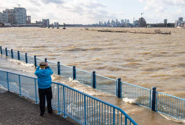 A man takes a photo of flooding at high tide on the Thames Path 