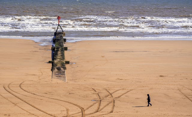 A person walks along the beach in sunny weather in Bridlington, Yorkshire