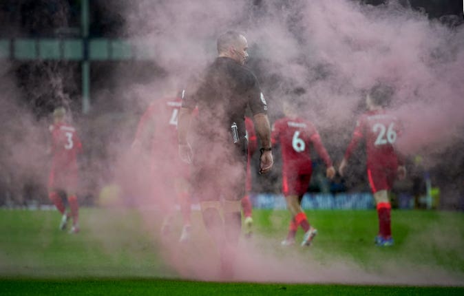 Referee Paul Tierney walks through smoke after a flare lands on the pitch as Liverpool celebrate their third goal 