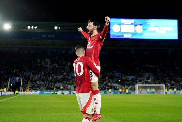 Bruno Fernandes holds his arms up in the air in celebration while being carried by Diogo Dalot