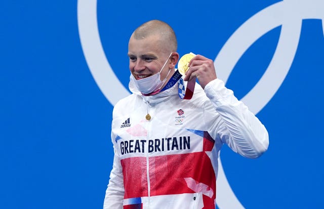 Adam Peaty, wearing a face mask, holds up his Olympic gold medal on the podium in Tokyo