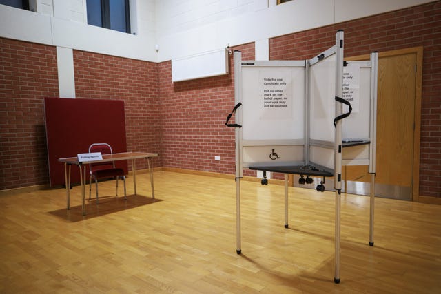 The interior of a polling station, with a white voting booth in the middle and a desk with chair at one end