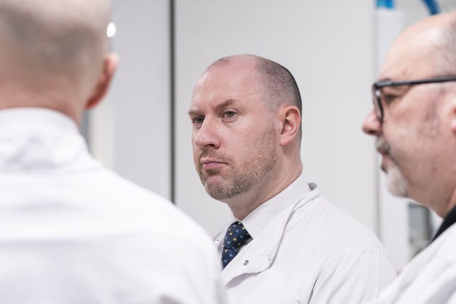 Neil Gray wearing a white medical coat, standing between two other men