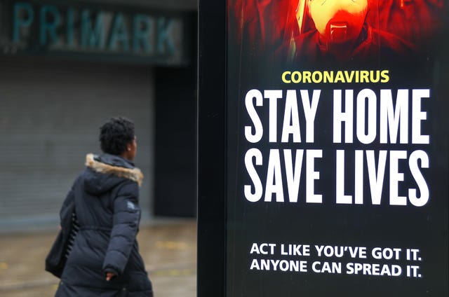 A person walks past a Stay Home Save Lives sign on Commercial Road in Portsmouth