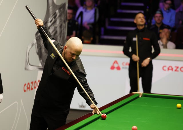 Luca Brecel plays from an awkward position on the side cushion as David Gilbert looks on
