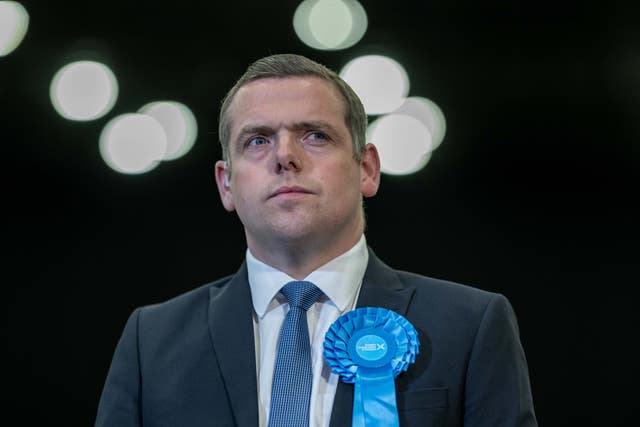 Douglas Ross stands with a Tory rosette on his suit jacket