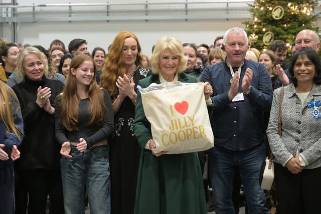 Queen Camilla holds a tote bag with the name of Jilly Cooper on it who wrote the original books entitled The Rivals as she poses with members of the cast and crew during a visit to the set of the series Rivals in Bristol