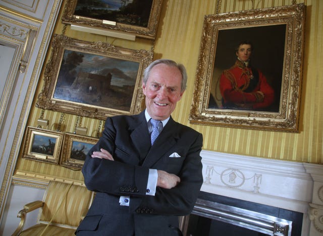 Charles Wellesley, Duke of Wellington, with arms folded in front of a portrait of his ancestor who won the Battle of Waterloo, in a similar pose.