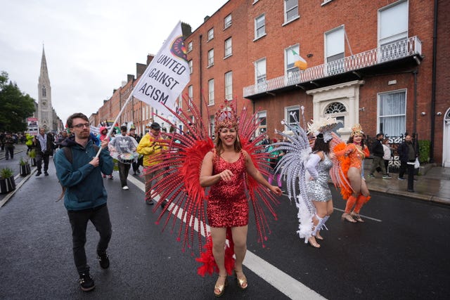 Women in carnival costumes and a man holding a flag which reads 'United Against Racism'
