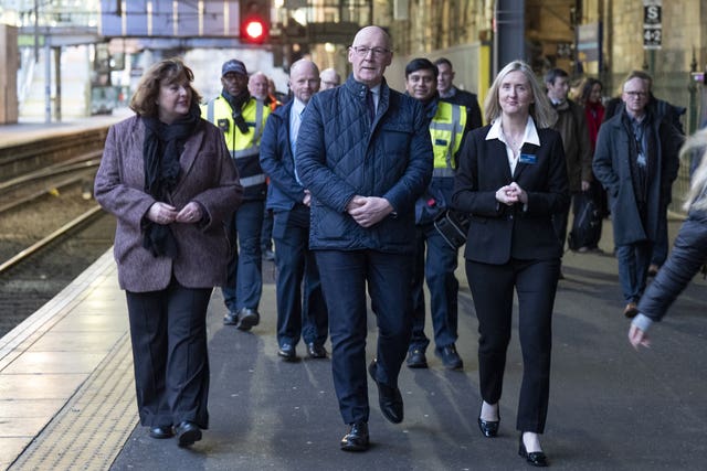 John Swinney in the centre of a group walking along a train station platform