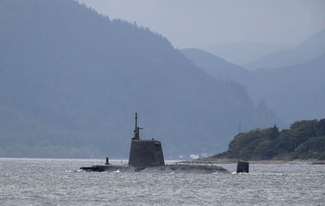 Submarine sailing in waters close to shore, with mountains in the background