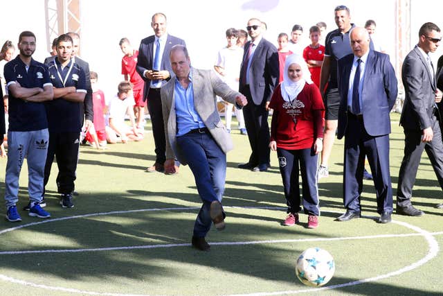Prince of Wales kicks a football while being watched by officials 