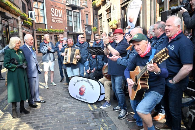 Charles and Camilla listen to the Causeway Shantymen during a visit to Commercial Court, Belfast