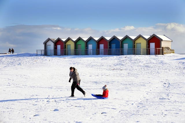 A woman pulls a child on a sledge through the snow beside the beach huts at Blyth in Northumberland
