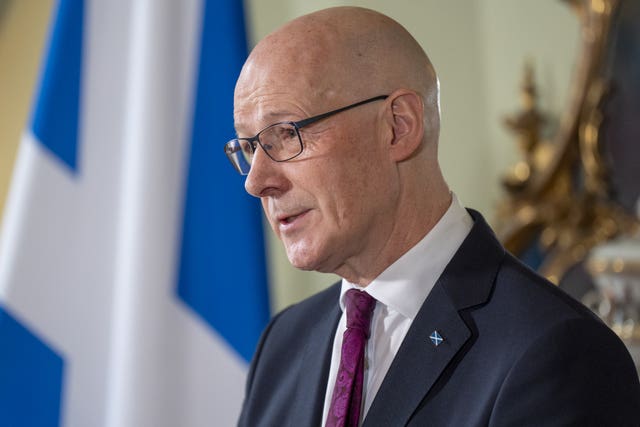 Side view of John Swinney speaking, with a Scottish flag in the background