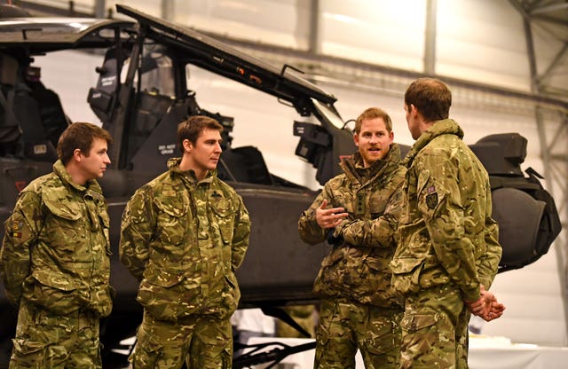 Harry talking to service personnel with an Apache helicopter in the background