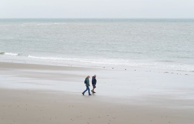 A couple walk along an overcast beach in Folkestone, Kent