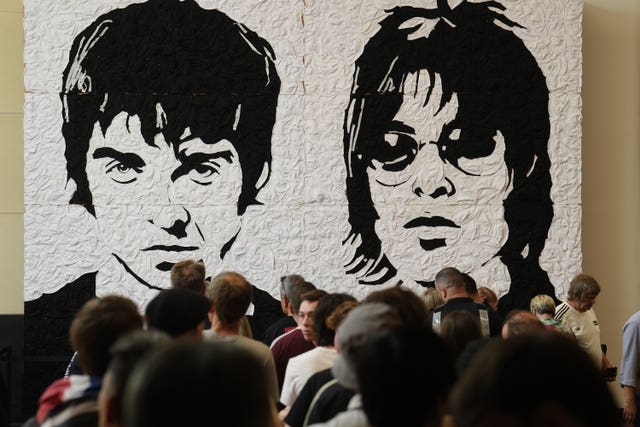 Oasis fans take photos in front of the Wonder Wall – a mural by Welsh artist Nathan Wyburn made out of 3,000 black and white bucket hats depicting Liam and Noel Gallagher