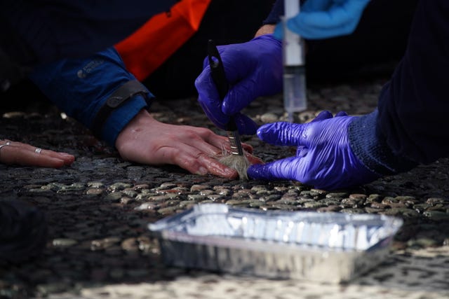 Police teams use a fluid de-bonding agent to unglue the the hands of protesters who stuck themselves to a road in Manchester