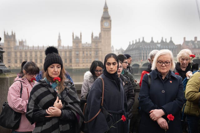 People holding roses during a moment of reflection with the Houses of Parliament in the background