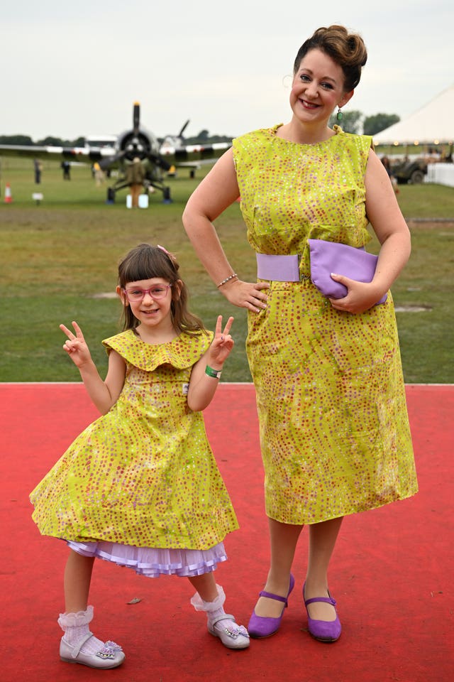 A woman and a young girl wearing matching red dresses pose on the red carpet