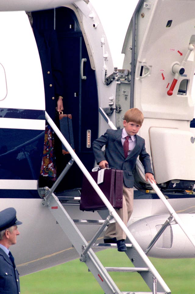 Harry, aged six, dressed in a suit and tie carries a briefcase down the down the steps of a plane in Scotland 