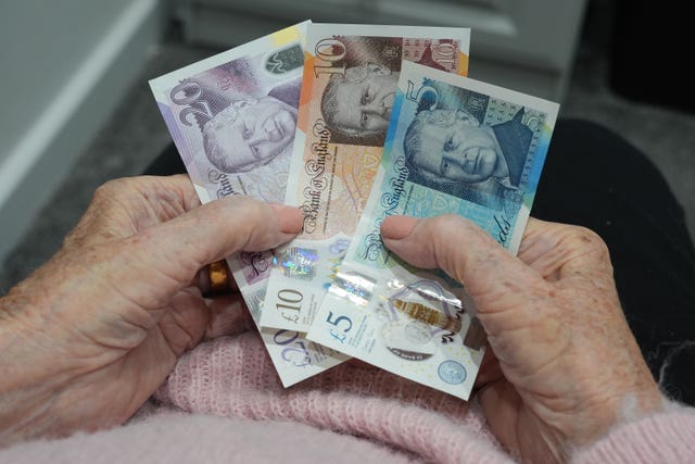 An old age pensioner holding bank notes at home in Essex 