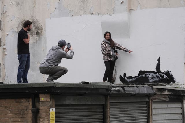 A person takes a photograph of a Banksy artwork