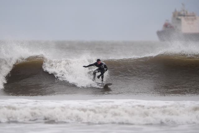 A surfer catches a wave in the wind at Tynemouth Longsands on the north east coast of England