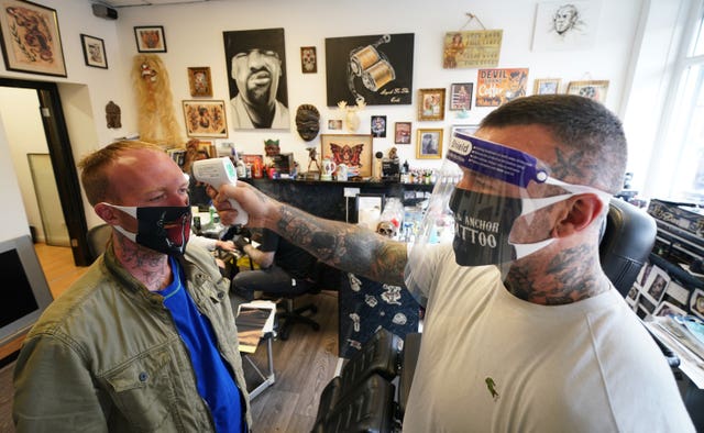 Tattoo artist Dan Ridgewell, 41, takes the temperature of a customer at the Axe & Anchor tattoo shop in North Shields, North Tyneside as they reopen to customers on following the easing of lockdown restrictions in England