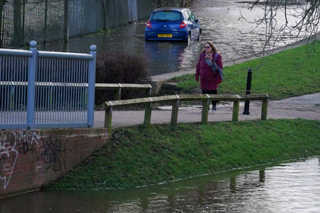 A woman walks past a stranded vehicle close to the flooded Worcester racecourse