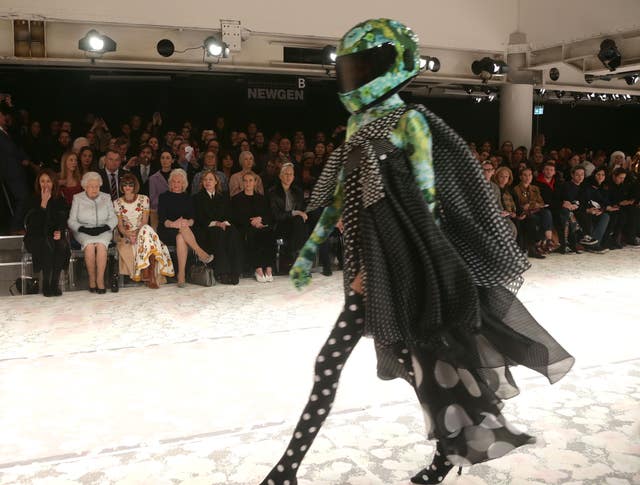 The Queen watches some of the more colourful outfits from Richard Quinn’s runway show (Yui Mok/PA)