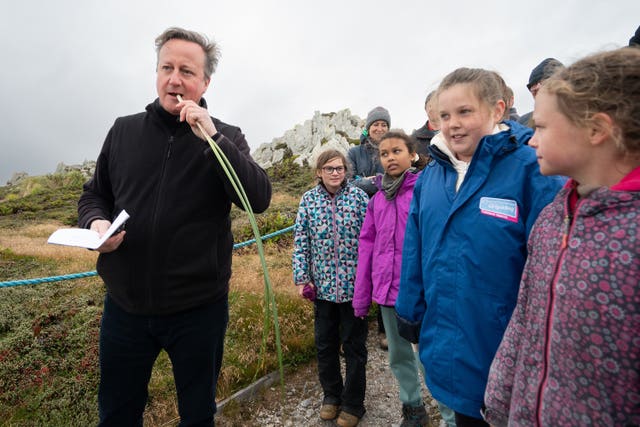 Lord Cameron tries eating some edible grass with local school children at Gypsy Cove