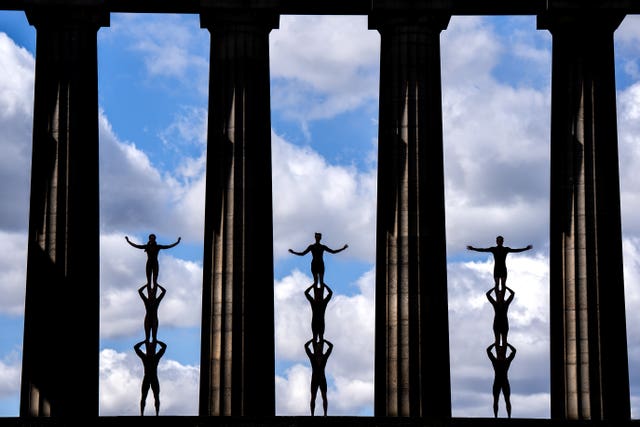 Three lots of three people standing on top of each other, in between large stone columns