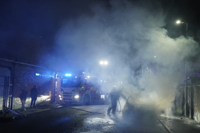 Firefighters tend to a burning police car burns as officers are deployed on the streets of Hartlepool following a violent protest 