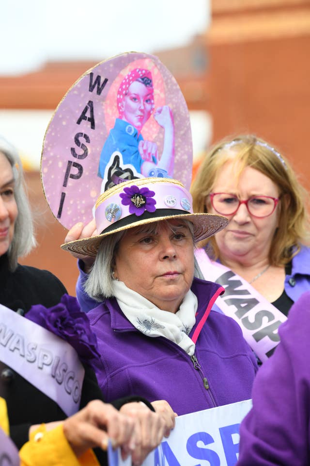 A woman dressed in purple and wearing a hat with a purple band in front of purple banners calling for Waspi women to be compensated 