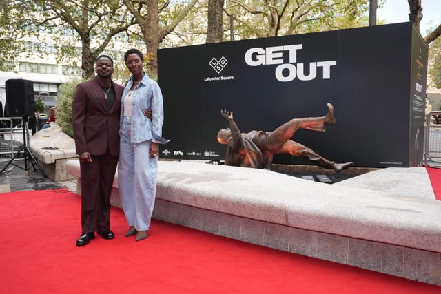 Jodie Turner-Smith and Daniel Kaluuya stand next to the statue of a scene from Get Out