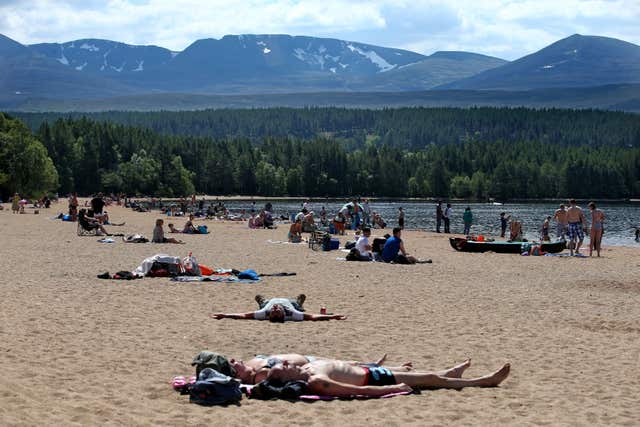 The last snow on the Cairngorms as sunbathers lie in the foreground (Jane Barlow/PA)