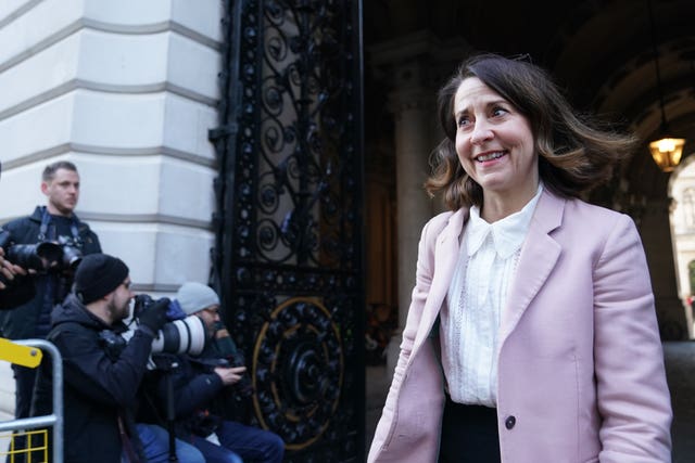 Liz Kendall smiling as she exits a building, with a group of photographers nearby